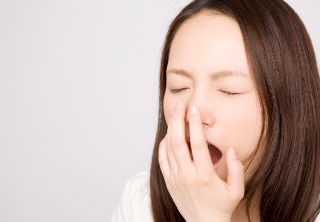 あくびをし口に手を当てる女性