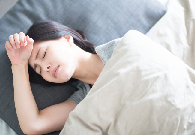 寝苦しそうに布団で寝ている若い女性